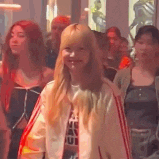 a woman in a pink jacket is standing in a crowd of people in a room .