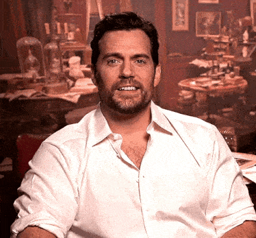 a man with a beard is wearing a white shirt and smiling while sitting in front of a table .