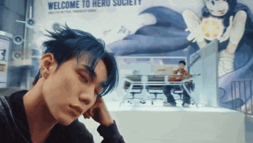 a man with blue hair is looking down in front of a welcome to hero society sign