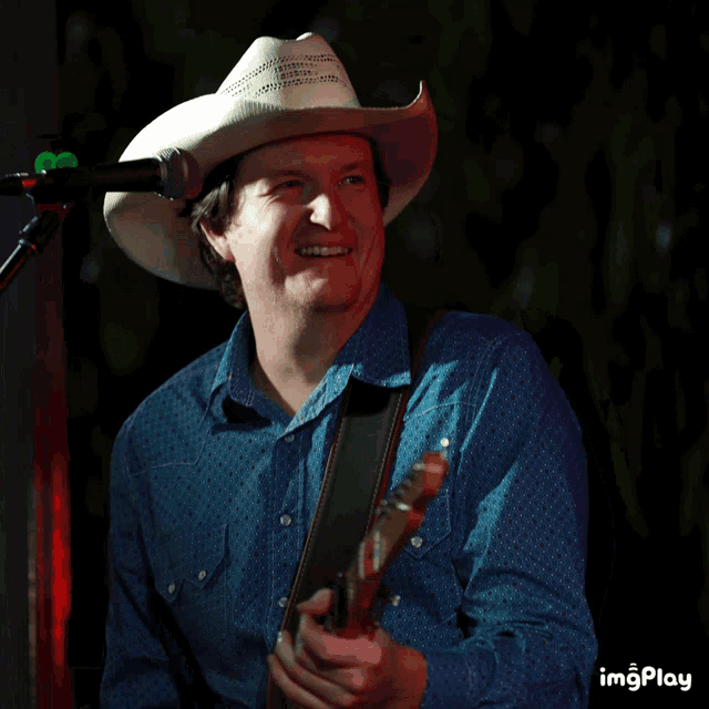 a man wearing a cowboy hat is playing a guitar and smiling