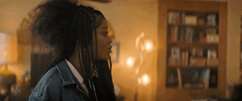 a woman with braids is standing in front of a bookshelf in a room .