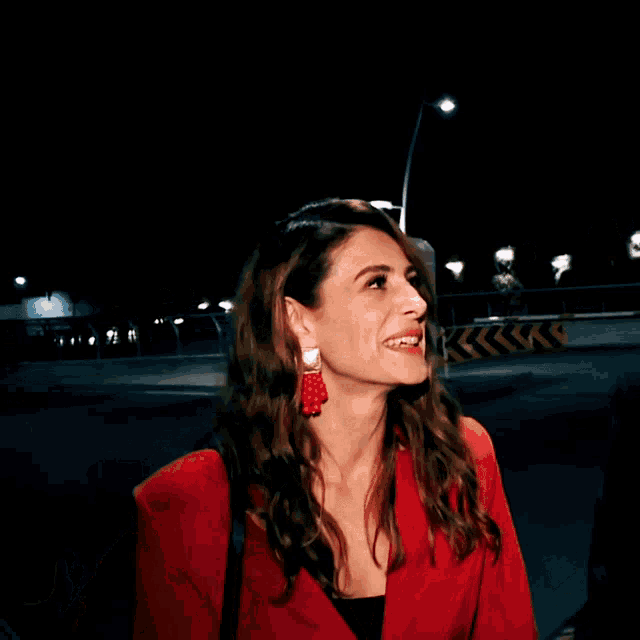 a woman in a red jacket and red earrings smiles