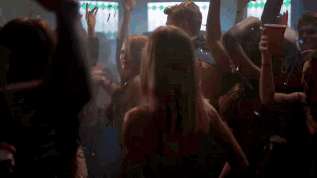 a group of people are dancing in a dark room with a woman holding a red cup