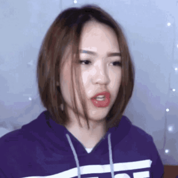 a young woman wearing a purple hoodie and red lipstick is making a funny face .