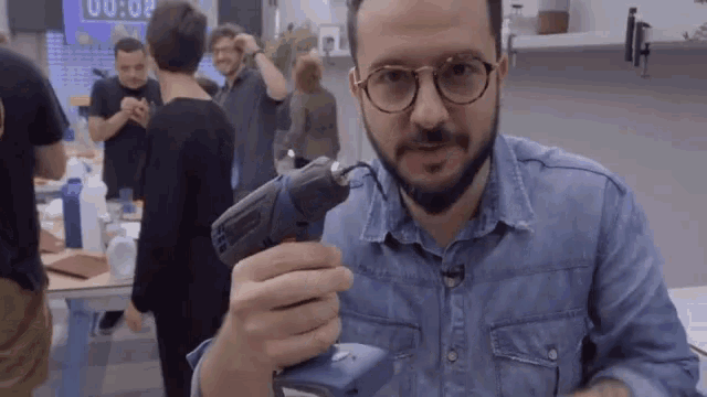 a man in a blue shirt holds a drill in front of a sign that says 00:00