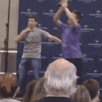 two men are standing in front of a crowd holding microphones and dancing .