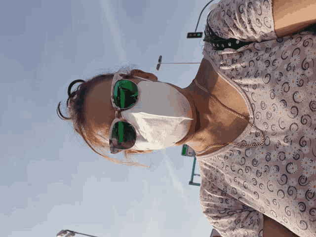 a woman wearing a face mask and sunglasses stands in front of a green light