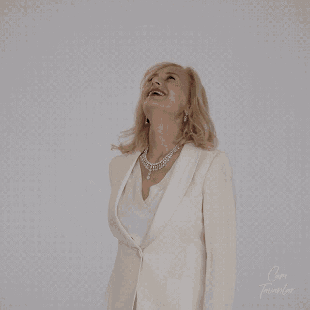 a woman in a white suit is laughing in front of a white background with the word coma written below her