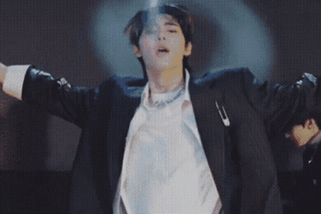 a man in a suit and white shirt is dancing on a stage with his arms outstretched .