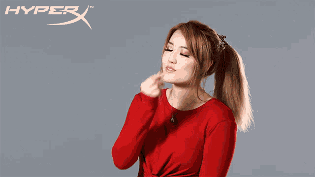 a woman in a red top is blowing a kiss in front of a hyperx logo
