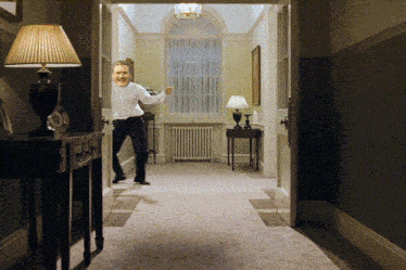 a man in a white shirt is dancing in a hallway with a lamp