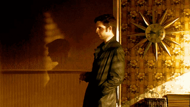 a man in a black coat stands in front of a clock that shows the time as 4:20