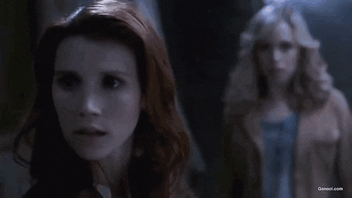 a woman with red hair is looking at the camera while another woman stands behind her .