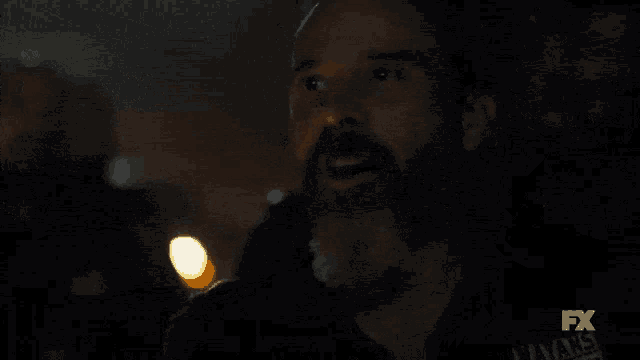 a man with a beard and mustache is standing in the dark looking up .