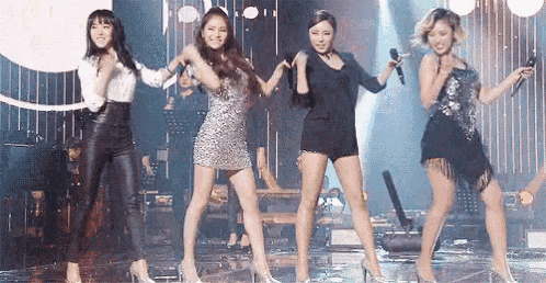 a group of women are dancing on a stage with microphones .