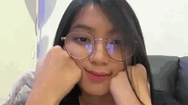 a young woman wearing glasses is sitting on a couch with her hands on her face .