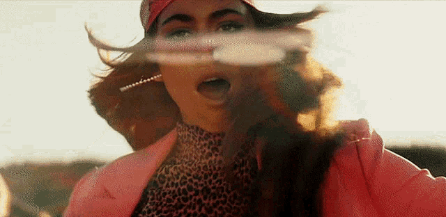 a woman wearing a pink jacket and a leopard print top is screaming with her mouth open .