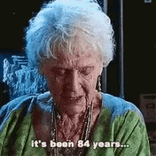 an elderly woman with white hair is wearing a green shirt and necklace and says `` it 's been 84 years ... ''