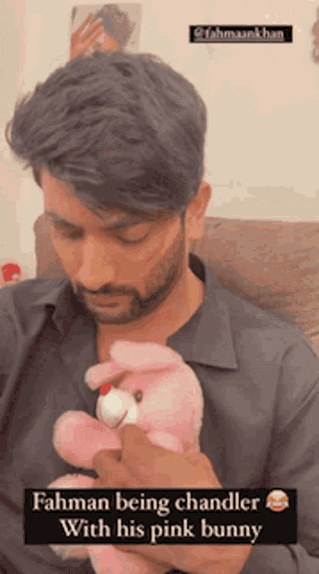 a man is holding a pink stuffed bunny and the caption says ' rahman being chandler with his pink bunny '