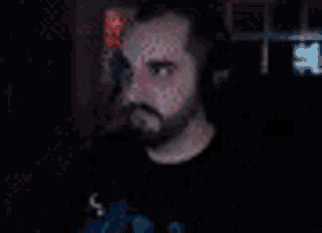 a man with a beard is standing in a dark room with a red light behind him .