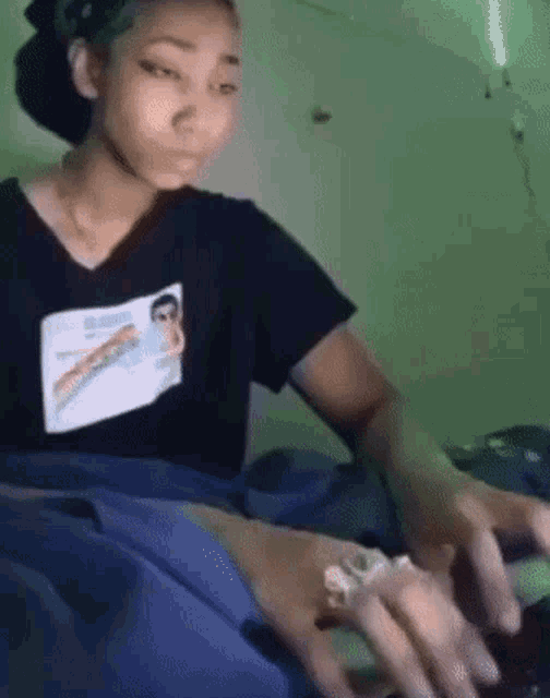 a woman in a black shirt with a picture of a woman on it is sitting on a bed .