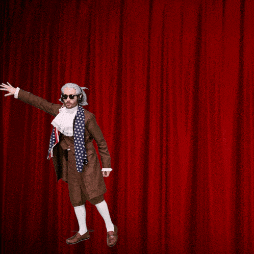a man in a suit and tie is standing on a red curtain