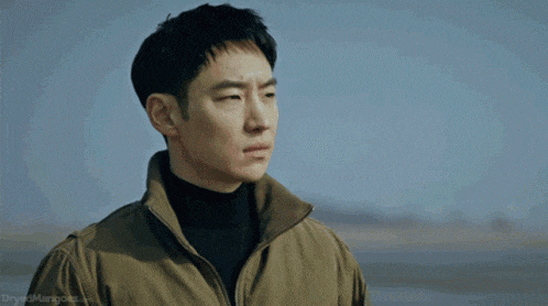 a man wearing a brown jacket and a black turtleneck looks to his left