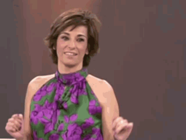 a woman in a purple and green dress is smiling and holding her fists up