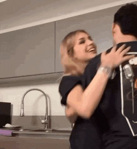 a man and a woman are hugging each other in a kitchen in front of a sink .