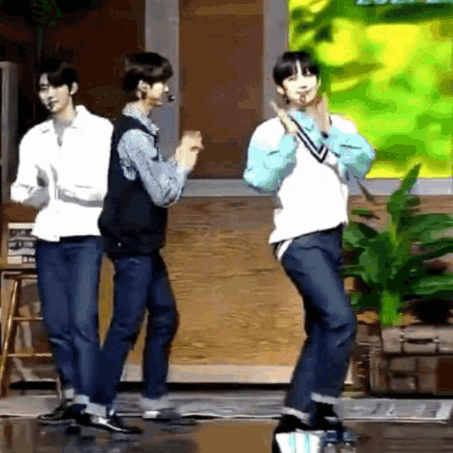 three young men are dancing on a stage in front of a plant .