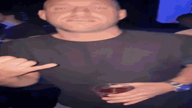 a man in a black shirt is giving a thumbs up and holding a glass