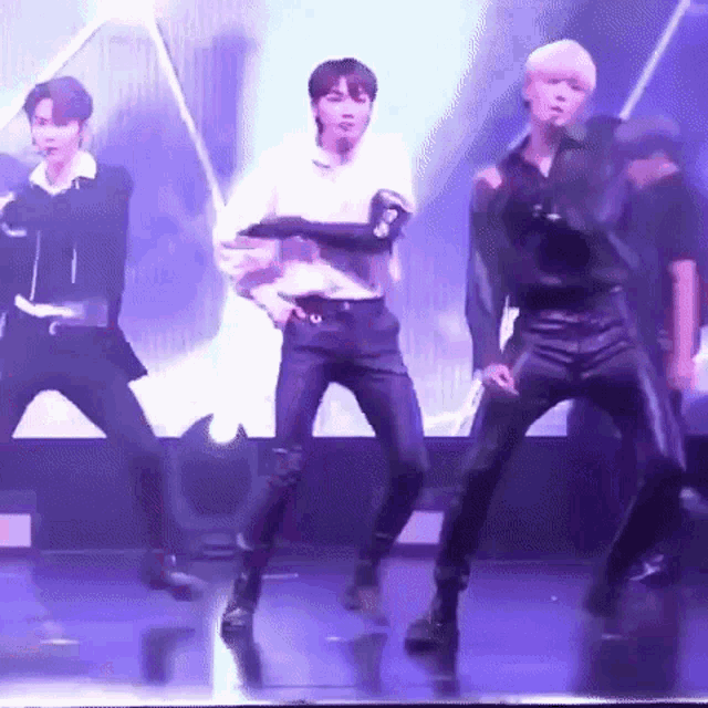 a group of young men are dancing on a stage in front of a purple light .