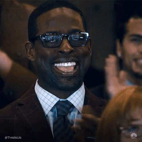 a man wearing glasses and a suit is laughing and clapping in a crowd .