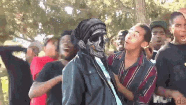 a group of people are standing around a man with a skull on his head .