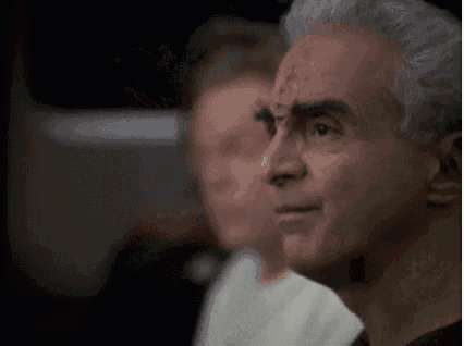 a man with gray hair and a cross on his forehead is sitting in front of a group of people .