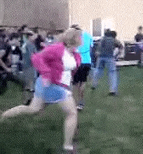 a woman in a pink jacket and blue skirt is running in the grass