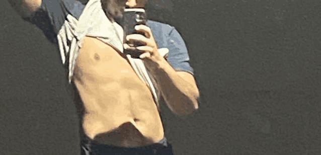 a shirtless man is taking a picture of himself in the mirror .