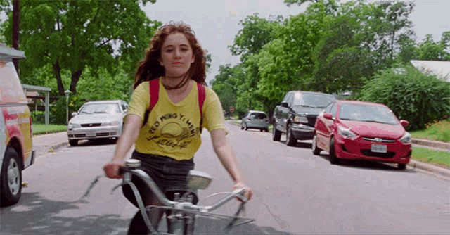 a girl is riding a bike down a street with a yellow shirt that says " ying ning yi ming "