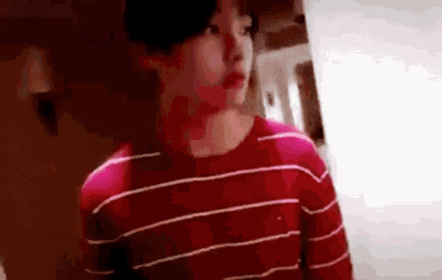 a young man is wearing a red striped shirt and standing in a room .