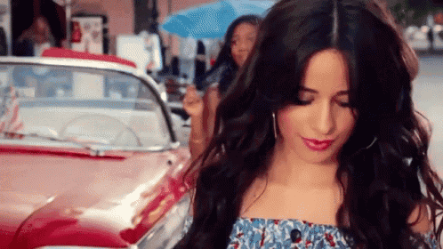 a woman with long hair is standing next to a red car .