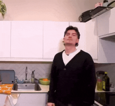 a man in a black sweater is standing in a kitchen with his eyes closed