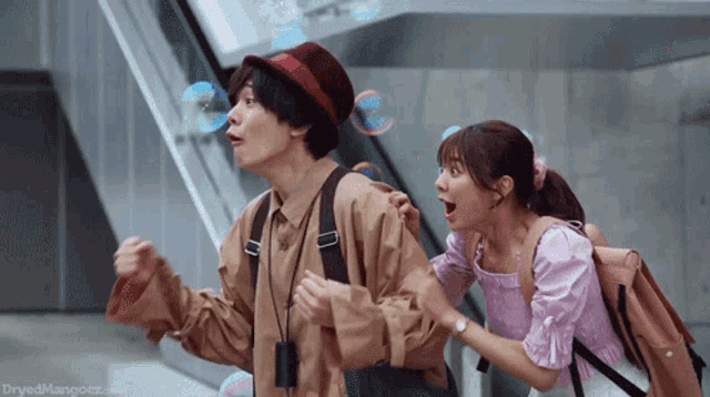 a man and a woman are playing with soap bubbles and the website dryedmangoez.com is visible