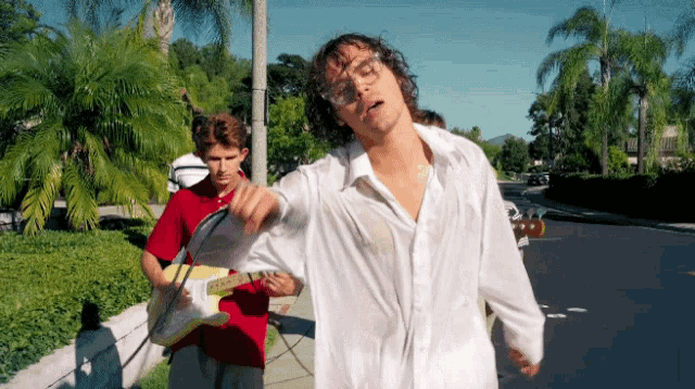 a man in a white shirt is standing on a sidewalk next to a man playing a guitar