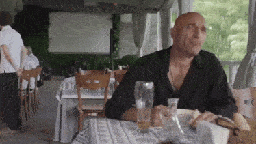 a bald man is sitting at a table in a restaurant with a glass of beer in front of him .