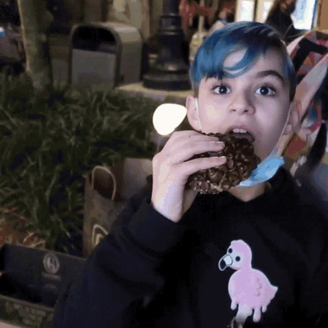 a boy with blue hair is eating a donut with a pink bird on it