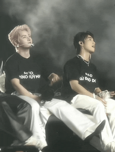 a man wearing a black shirt that says say 10 hung huynh sits next to another man