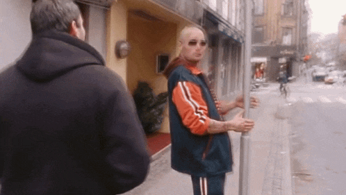 a man in a black hoodie is talking to a man in an orange and blue jacket