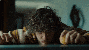 a man with curly hair is laying on a table with his head on the table