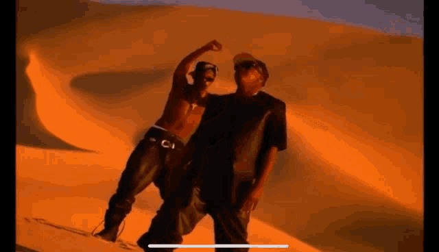 two men are standing next to each other in front of a sand dune in the desert .