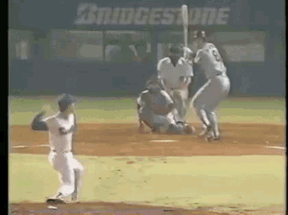 a baseball game is being played on a field with a bridgestone ad in the background .